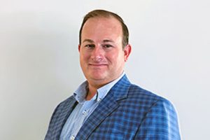 James Land in blue, plaid blazer over pale blue button up shirt.
