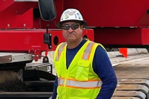 Jesus Nunez in front of a crane while wearing PPE.