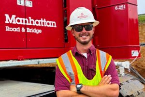 Isaac Brandstetter posing in front of a red Manhattan Road & Bridge Crane while wearing PPE.