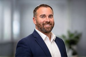 Nick Burt wearing dark blue blazer over white button up shirt.